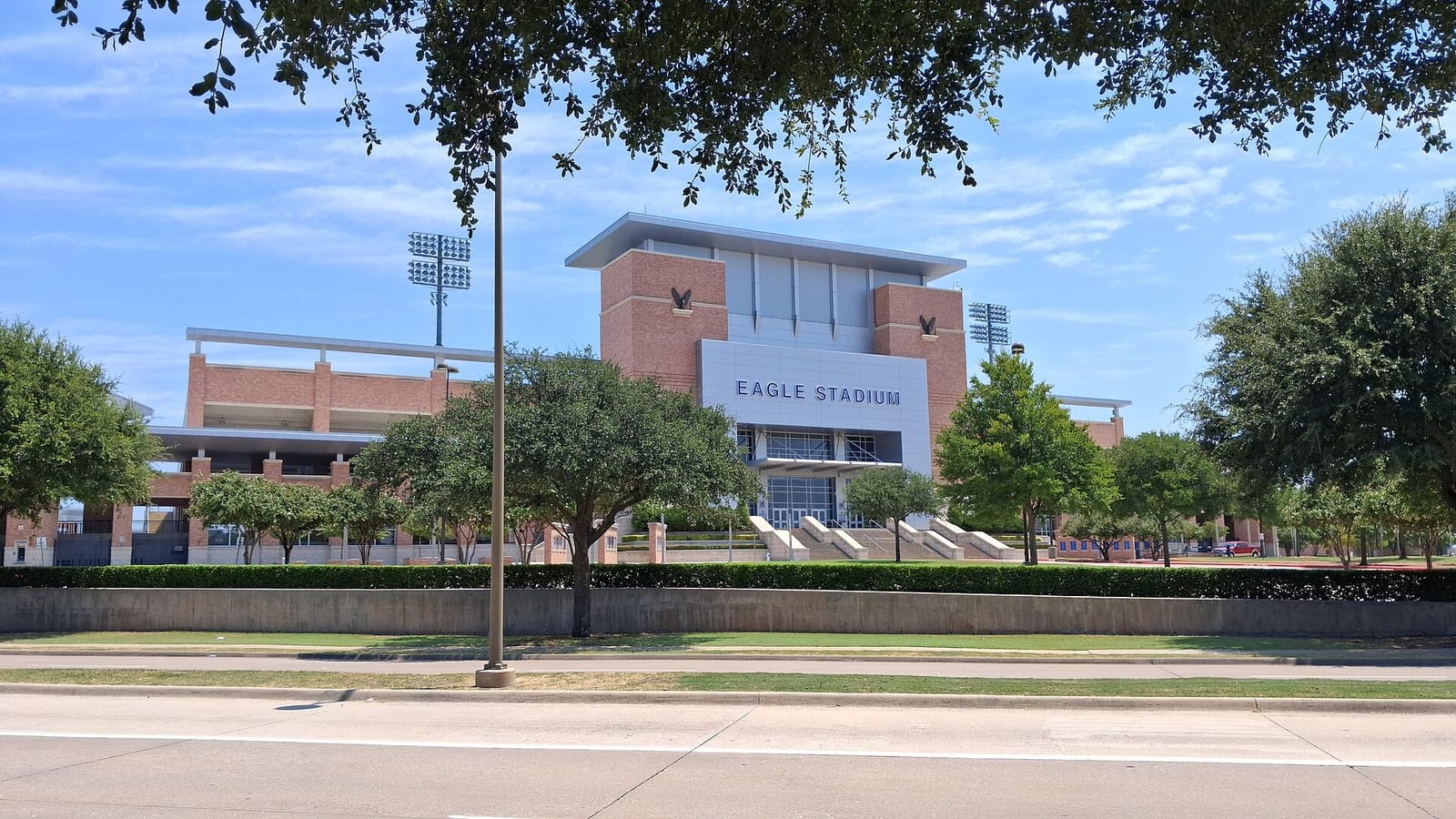 Eagle Stadium in Allen, Texas, the brick Allen ISD football stadium seen from the street behind a row of live oaks