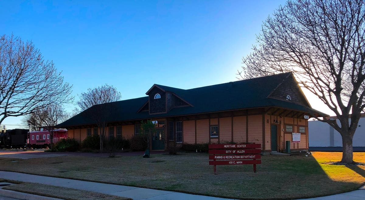 The Allen Heritage Center, a long single-story wood depot building with deep eaves and a red City of Allen sign at 100 East Main Street