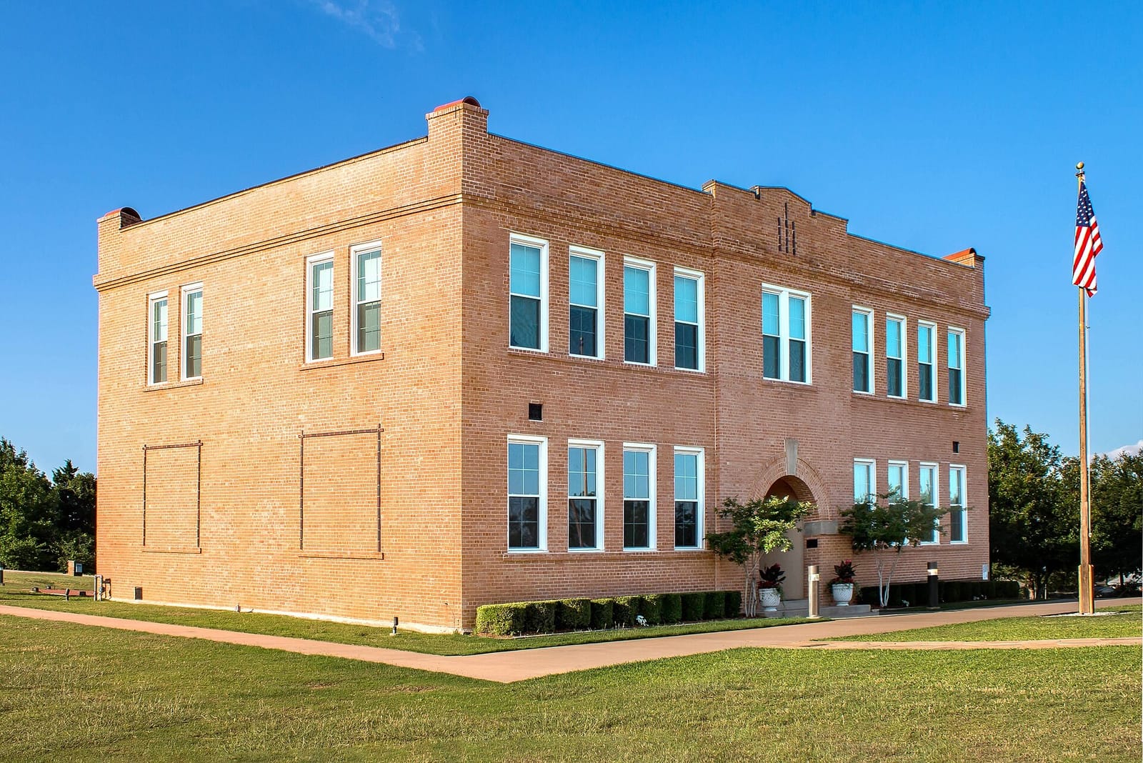 The two-story brick Old Bedford School at 2400 School Lane in Bedford, Texas, with tall white windows, an arched entry, and a flag on the lawn