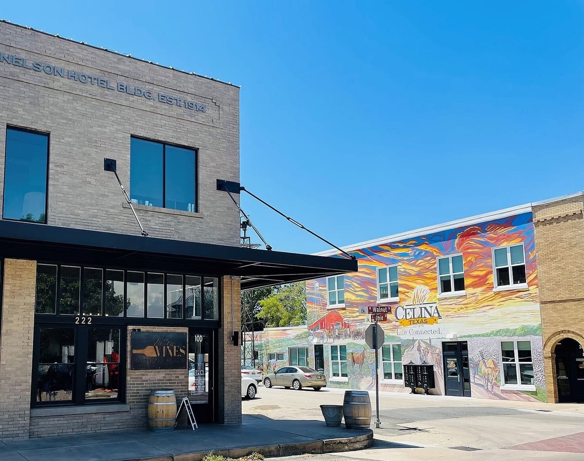 The Nelson Hotel building in Celina, a two-story tan brick corner building with a black steel canopy, beside a colorful mural of Celina's farm history