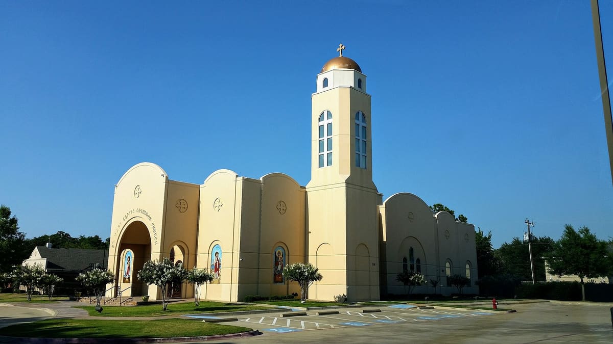 St. Mary Coptic Orthodox Church in Colleyville, a cream stucco church with arched gables, mosaic icons, and a bell tower topped by a gold dome and cross