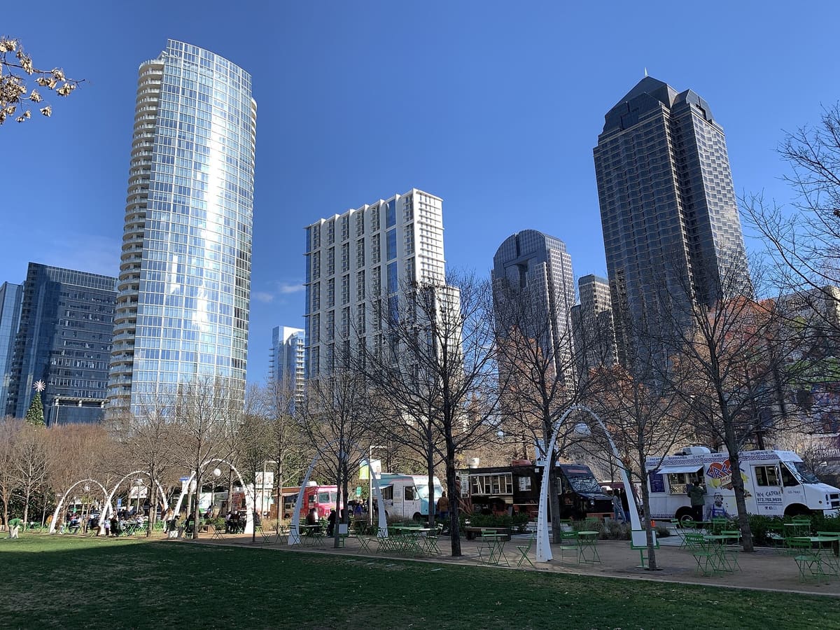 Klyde Warren Park lawn with food trucks, white arches, and Uptown towers behind on a clear day