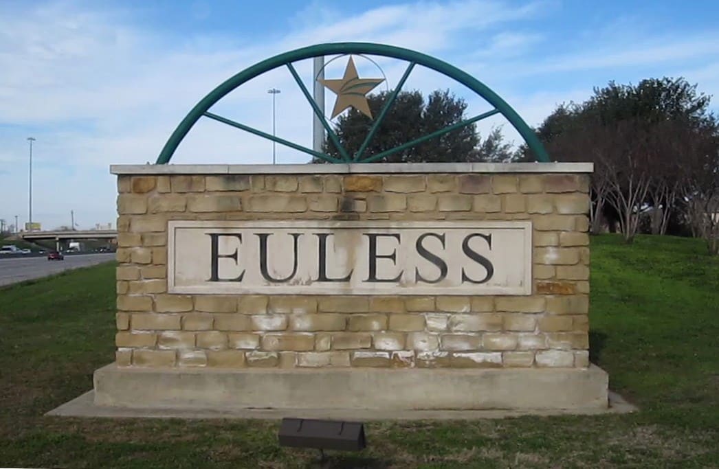 A stone Euless city monument sign with the city name carved in a limestone panel under a green wagon wheel arch and gold star, beside a highway