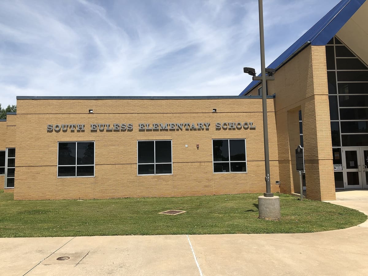 South Euless Elementary School, a tan brick building with steel lettering, a blue metal roof over a glass entry, and a Texas Historical Commission marker beside the front door