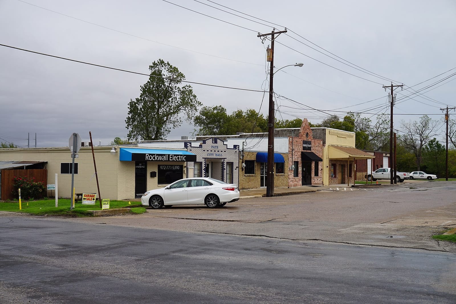 One-story brick storefronts on Fate Main Place in downtown Fate, Texas, including a white glazed brick building trimmed in blue and lettered Fate City Hall
