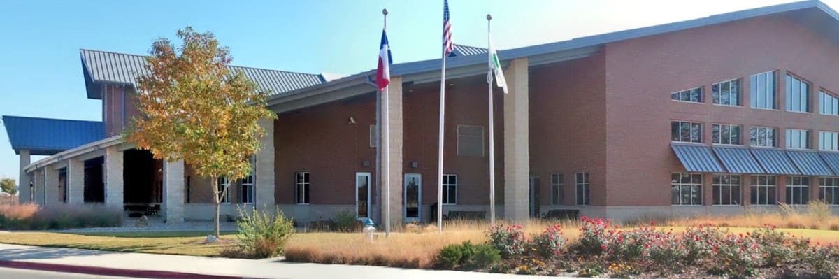 The Flower Mound Community Activity Center, a red brick building with tan stone columns, blue standing-seam metal roofs, and flagpoles out front