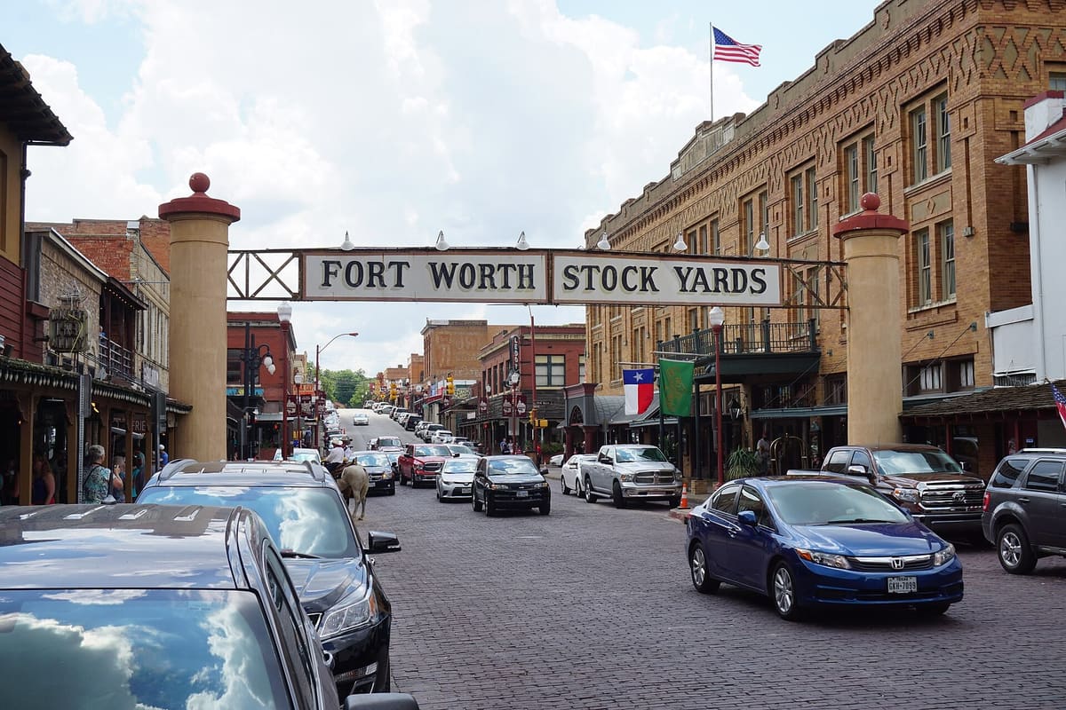 The Fort Worth Stock Yards sign arching over brick-paved Exchange Avenue, with historic brick buildings and the Stockyards Hotel on either side