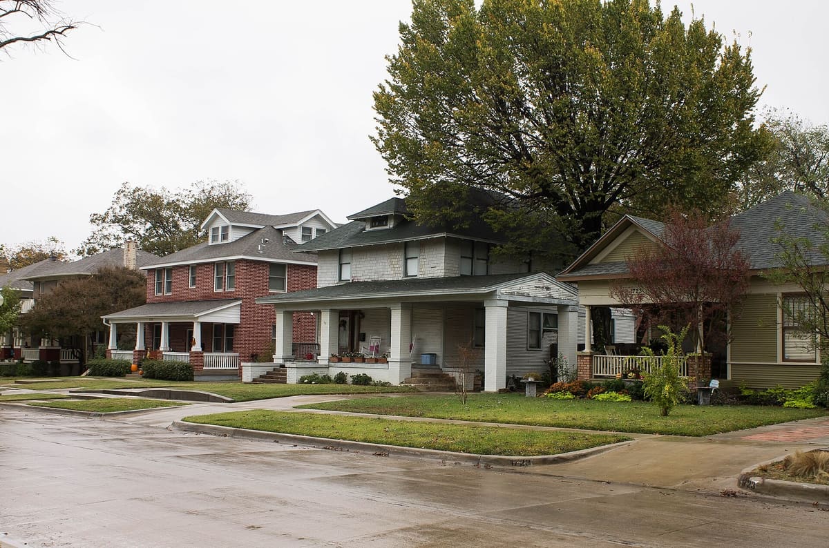 A row of early 1900s Fairmount houses in Fort Worth: a red brick foursquare, a white shingled foursquare with a deep porch, and a green bungalow