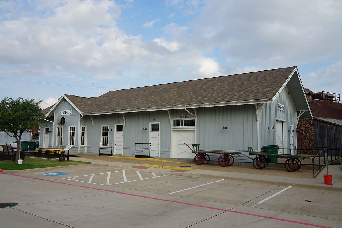 The board-and-batten Frisco railroad depot with FRISCO signs and antique baggage carts at the Frisco Heritage Center