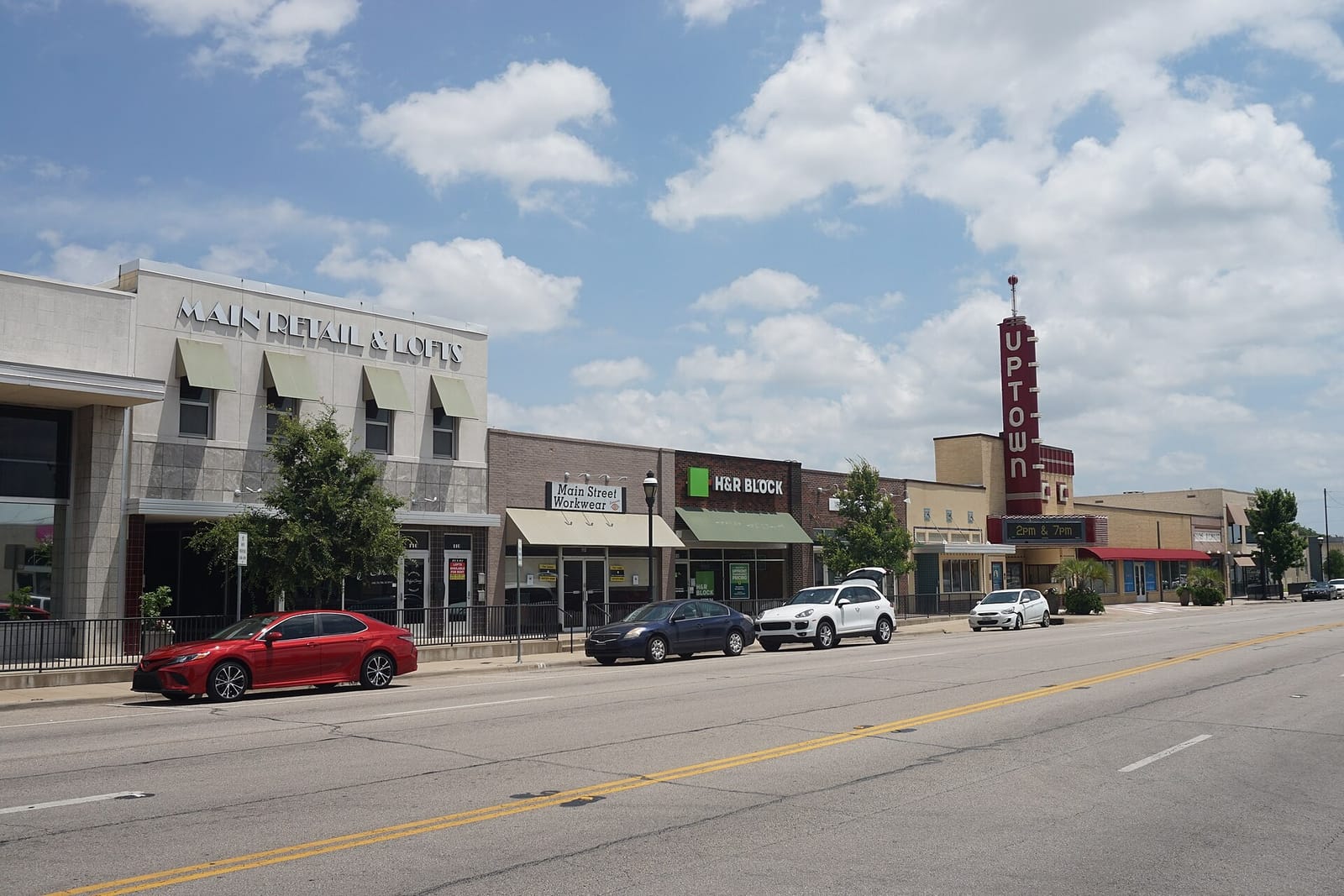 East Main Street in downtown Grand Prairie, Texas, with brick storefronts, the Main Retail and Lofts building, and the Uptown Theatre's red vertical sign under a summer sky