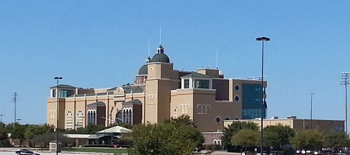 Lone Star Park's domed tan grandstand building in Grand Prairie under a clear blue sky, with trees and tall light poles in front