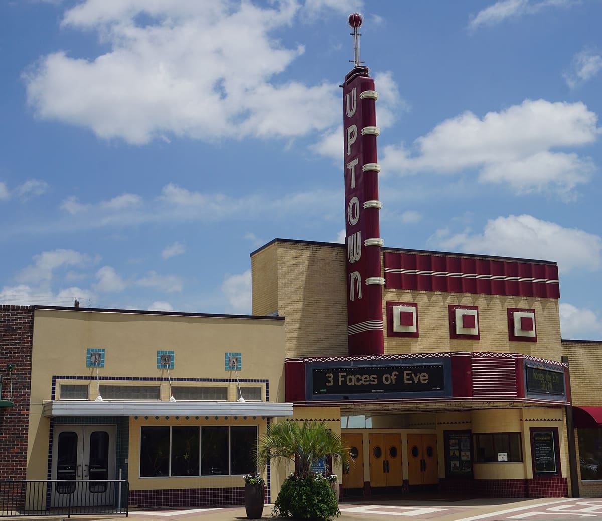 The Uptown Theatre on Main Street in Grand Prairie, a yellow brick Art Deco facade with a tall maroon vertical sign, a lit marquee, and wood entry doors