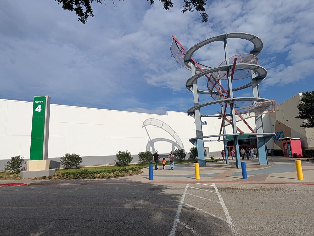 The Entry 4 entrance at Grapevine Mills, a long white mall wall with a green entry sign beside a tall steel ring sculpture over the doors