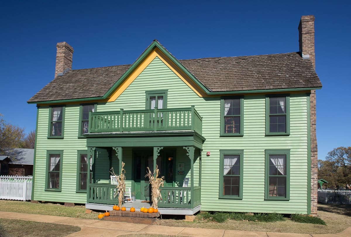 The two-story Nash farmhouse in Grapevine, a pale green clapboard I-house with dark green trim, a front porch and balcony, and brick chimneys at each end