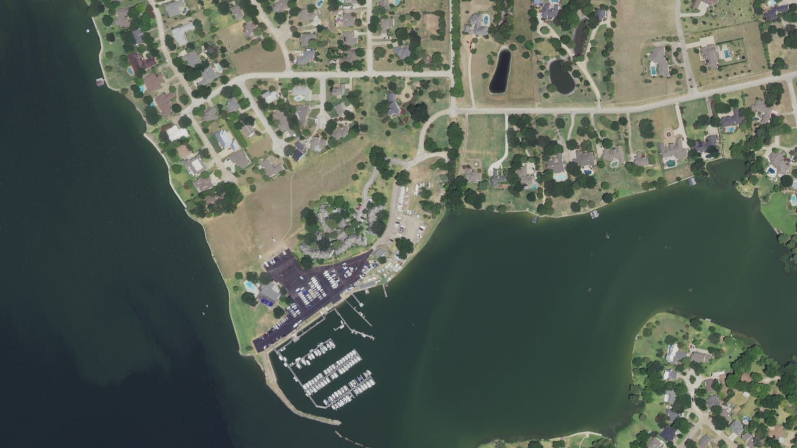 Aerial view of Rush Creek Yacht Club in Heath, Texas, with marina docks, a stone breakwater, and dry boat storage on Lake Ray Hubbard beside large wooded home lots