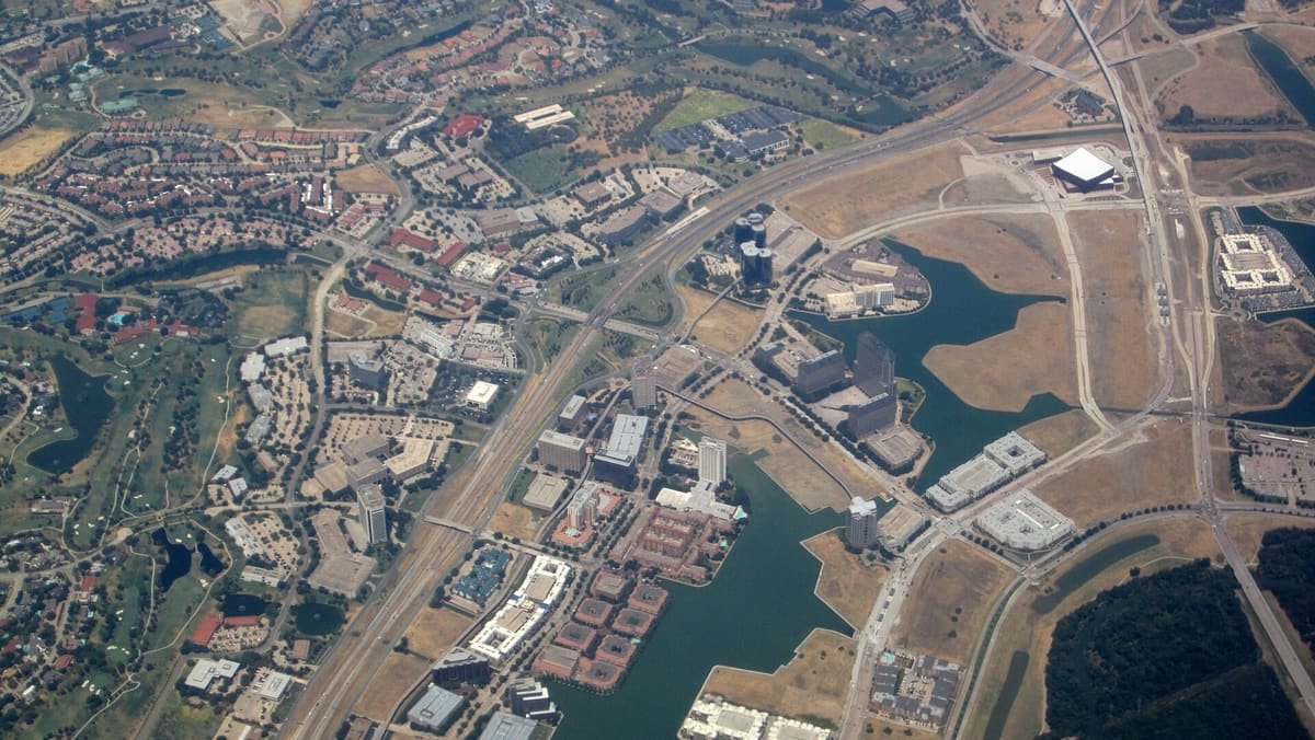 Aerial view of Las Colinas showing Lake Carolyn, canal-side buildings, and the office towers of the Urban Center beside the freeway