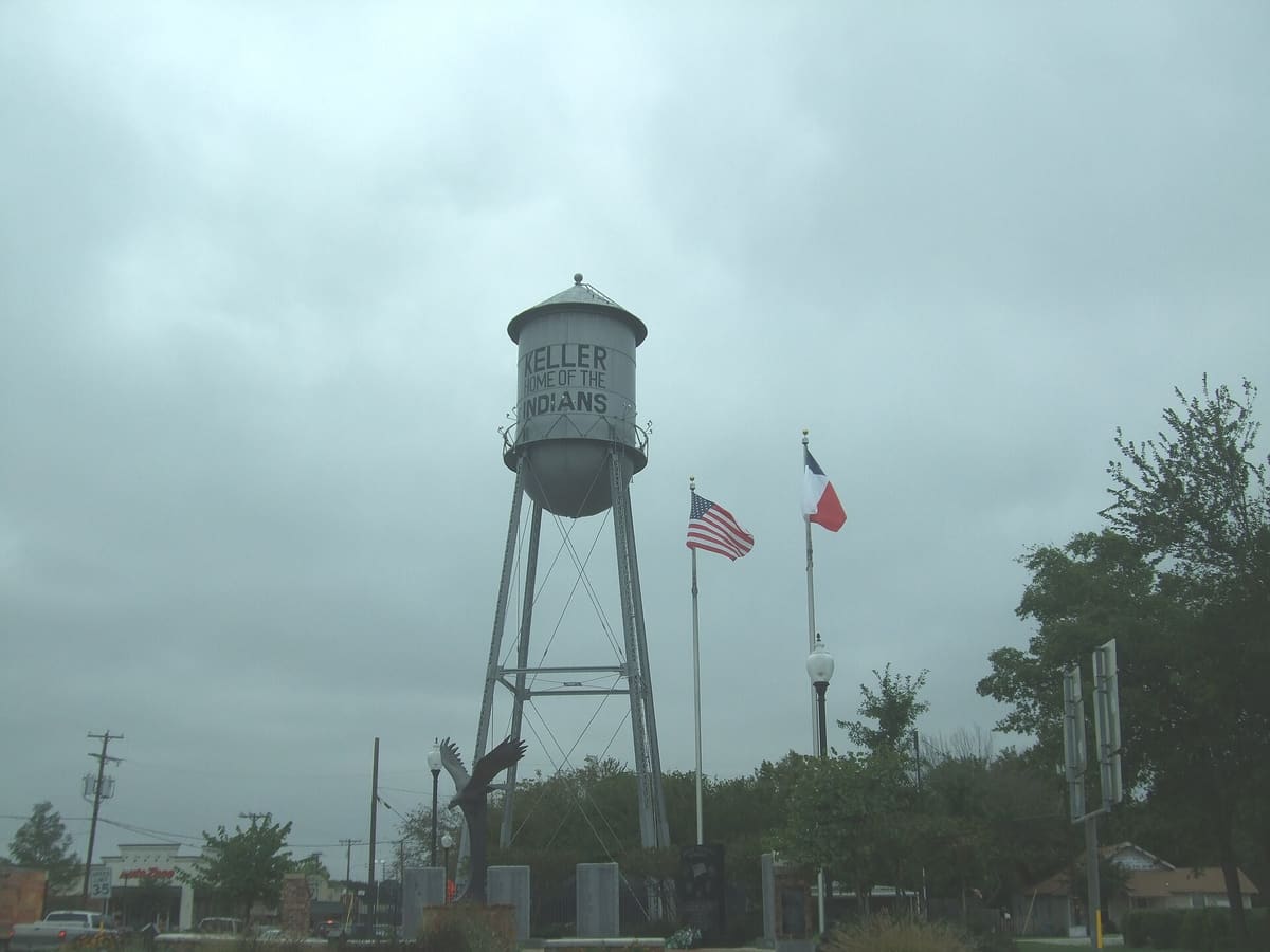 Keller's silver water tower painted Keller Home of the Indians, with American and Texas flags and the Veterans Memorial eagle sculpture at its base