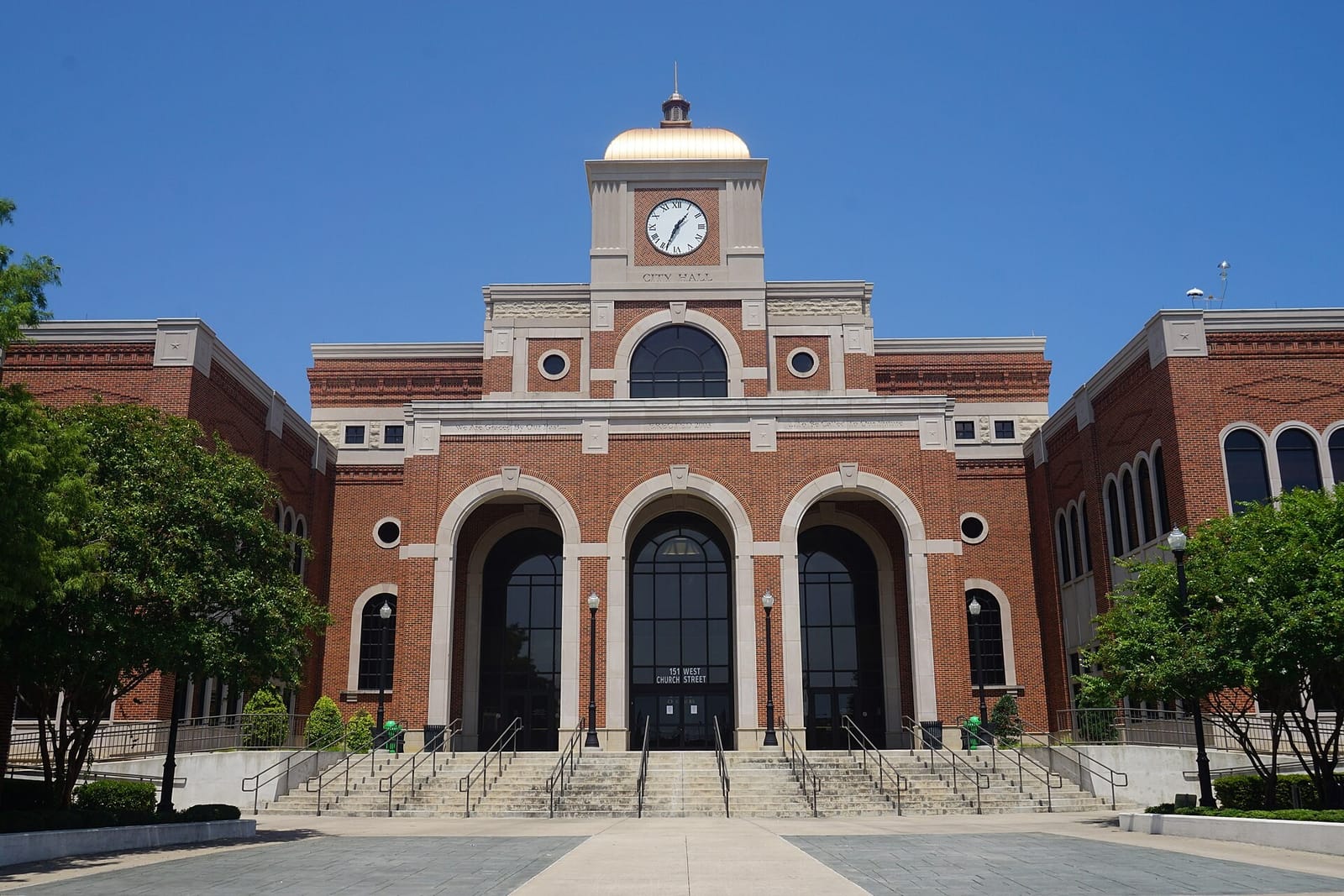 Lewisville City Hall at 151 West Church Street in Old Town, a red brick building with a clock tower, a gold dome, and three tall arched entrances