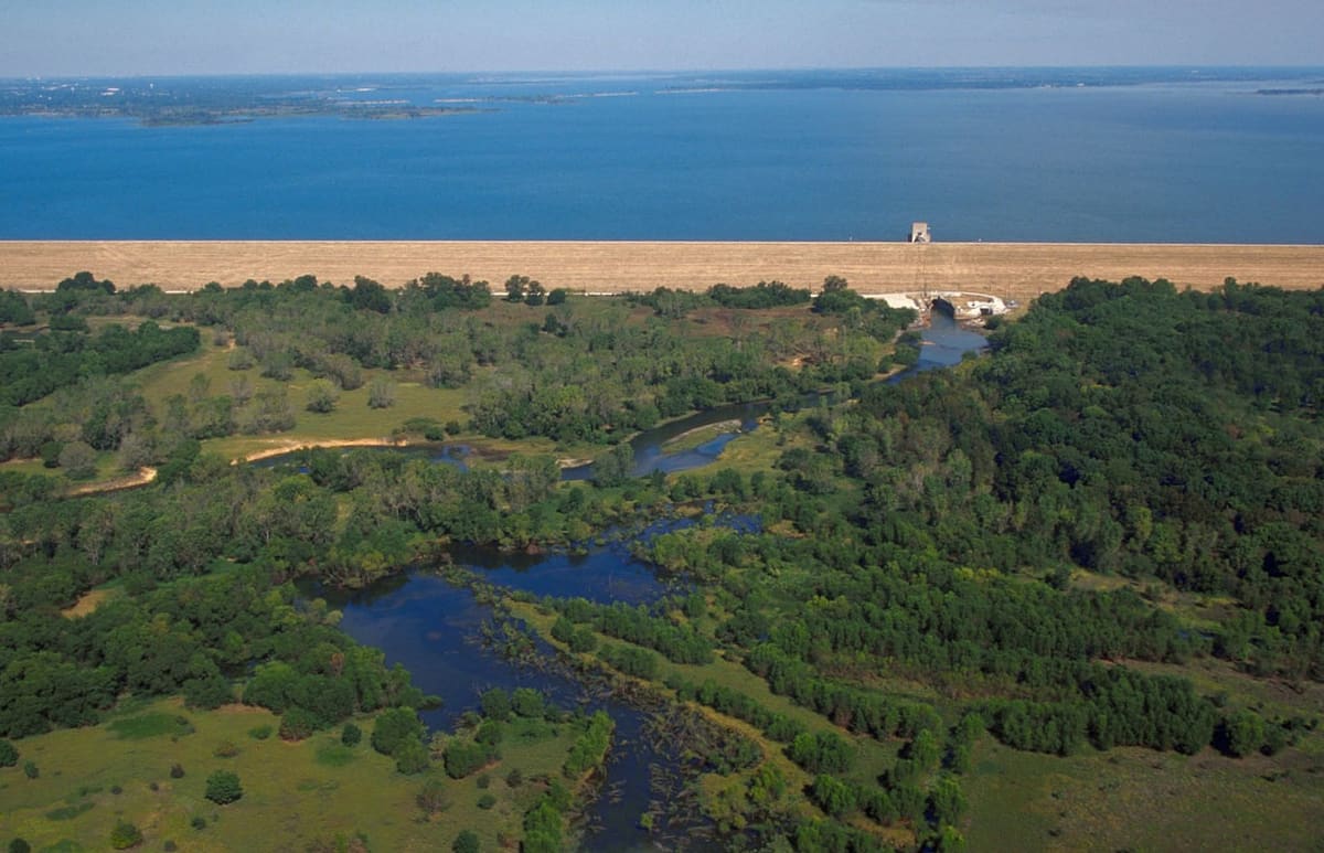Aerial view of Lewisville Lake and its long earthen dam, with the forested Elm Fork bottomland of the Lewisville Lake Environmental Learning Area spreading out below it