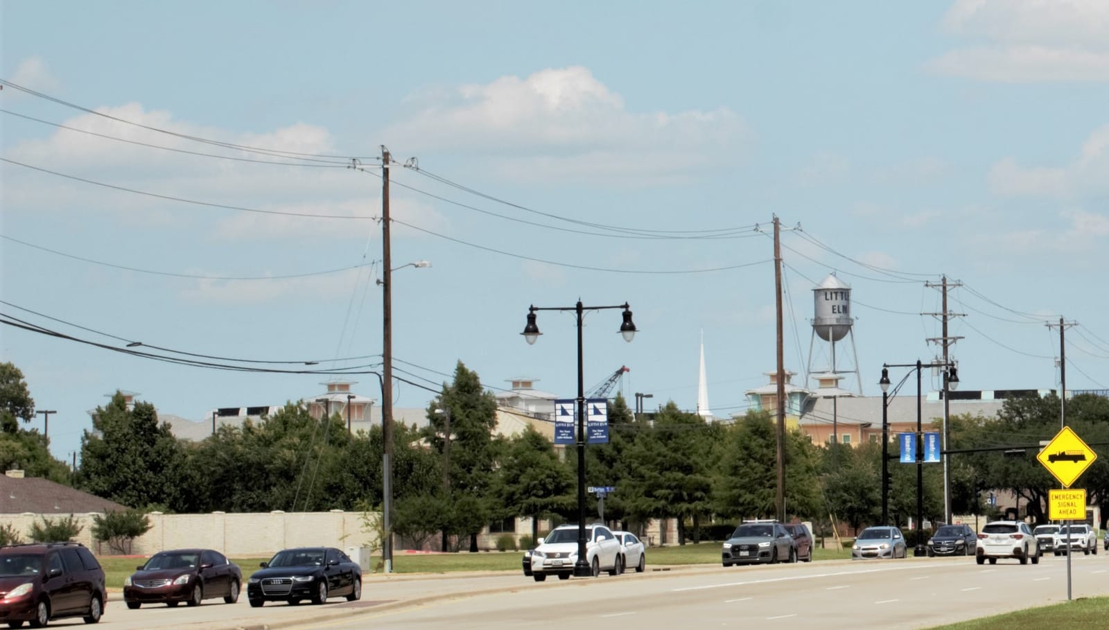 A street near Main Street in Little Elm, Texas, with Lakefront banners on the light poles and the silver LITTLE ELM water tower rising behind the trees