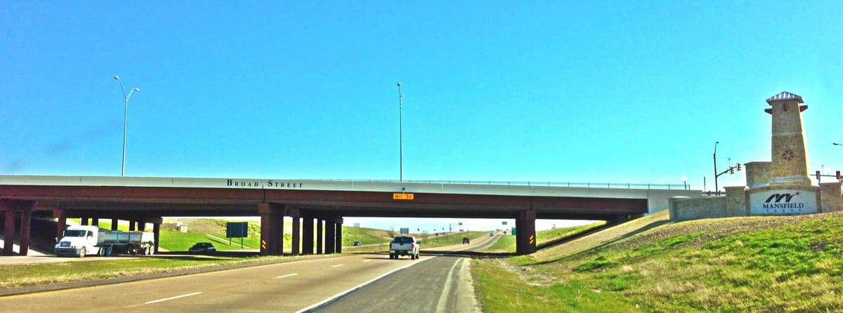US 287 southbound passing under the Broad Street overpass in Mansfield, with a stone Mansfield gateway tower on the grassy embankment