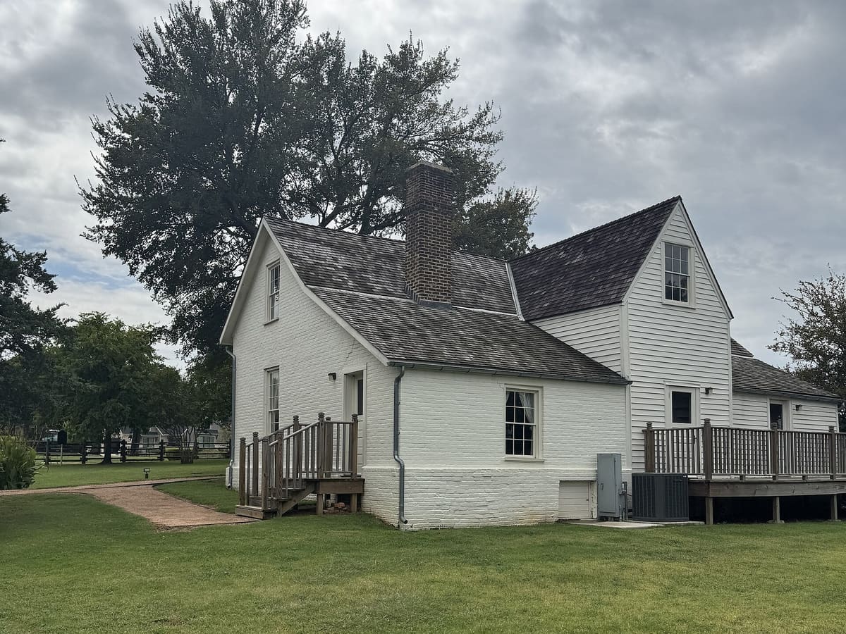 The Man House Museum in Mansfield, a painted white brick and clapboard house with a wood shingle roof, brick chimney, and wood deck under a large tree