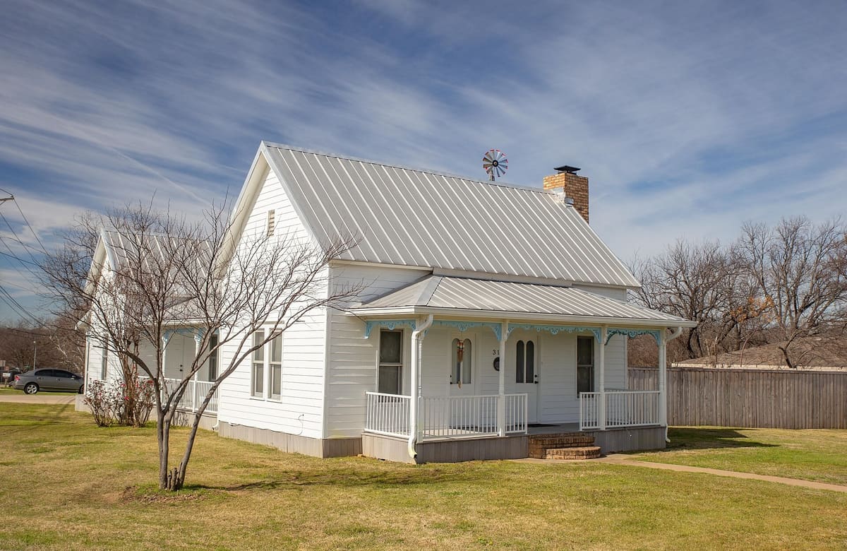 The Nugent-Hart House in Mansfield, a white one-story frame house with a standing seam metal roof, scrollwork porch brackets, and a brick chimney