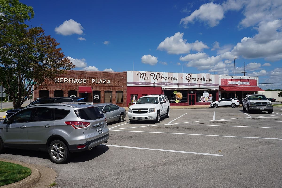 Heritage Plaza and the McWhorter Greenhaw building on Broad Street in downtown Mesquite, one-story brick and painted storefronts facing a parking lot