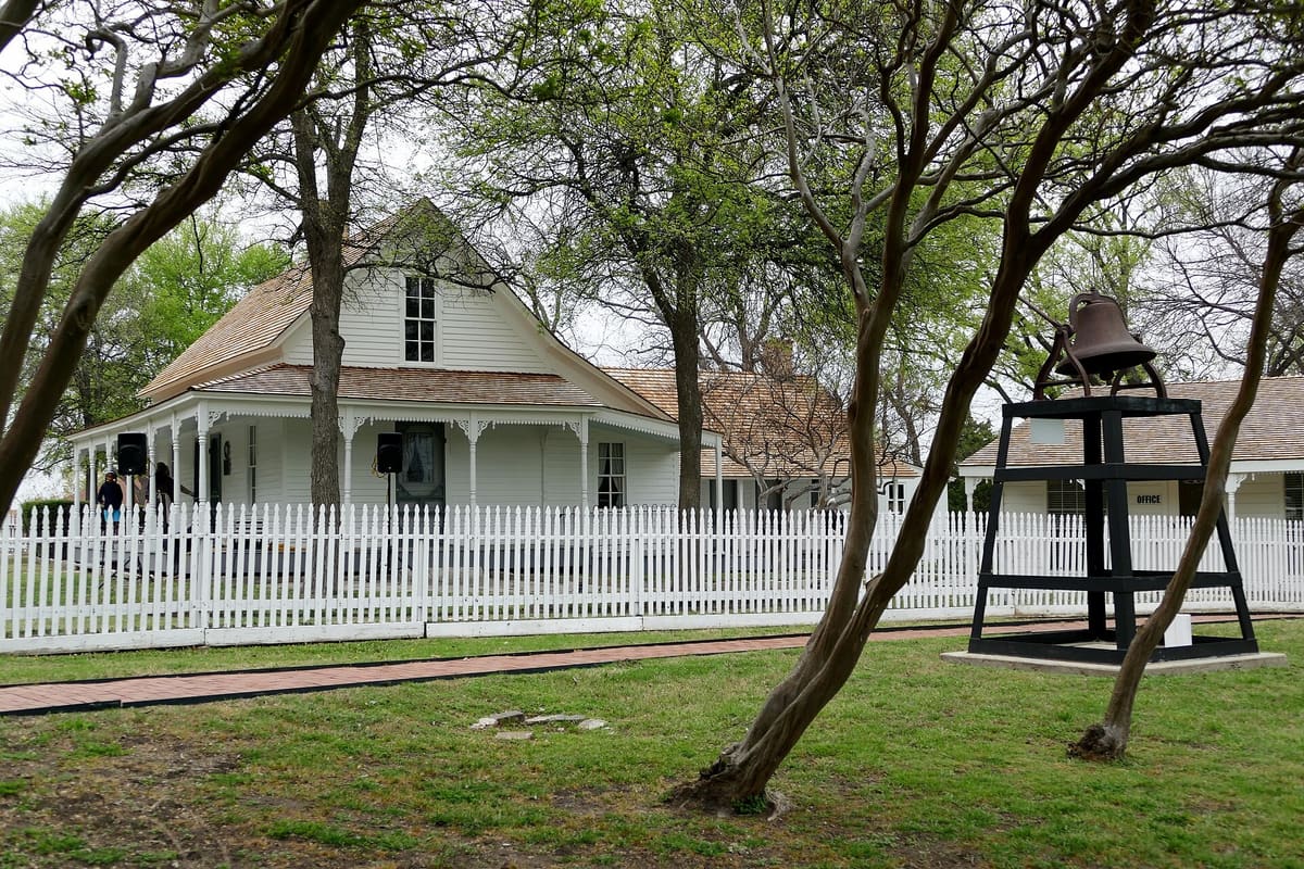 The Florence Ranch Homestead in Mesquite, a white frame farmhouse with a decorated front gallery behind a white picket fence and an iron bell on a black frame