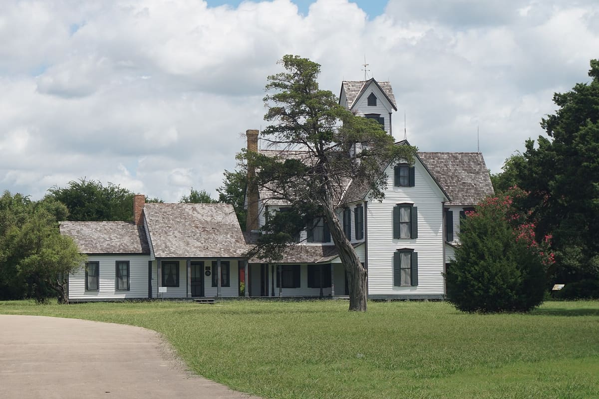 The white clapboard Lawrence farmhouse at Opal Lawrence Historical Park in Mesquite, with dark green shutters, a cedar shingle roof, and a square belvedere tower