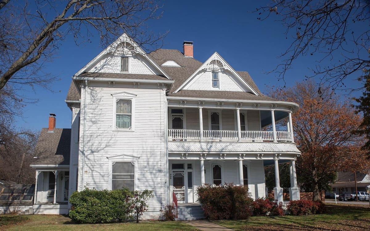 The white two-story Hawkins House in Midlothian with a wraparound two-level porch, gingerbread trim, and decorative gable vents