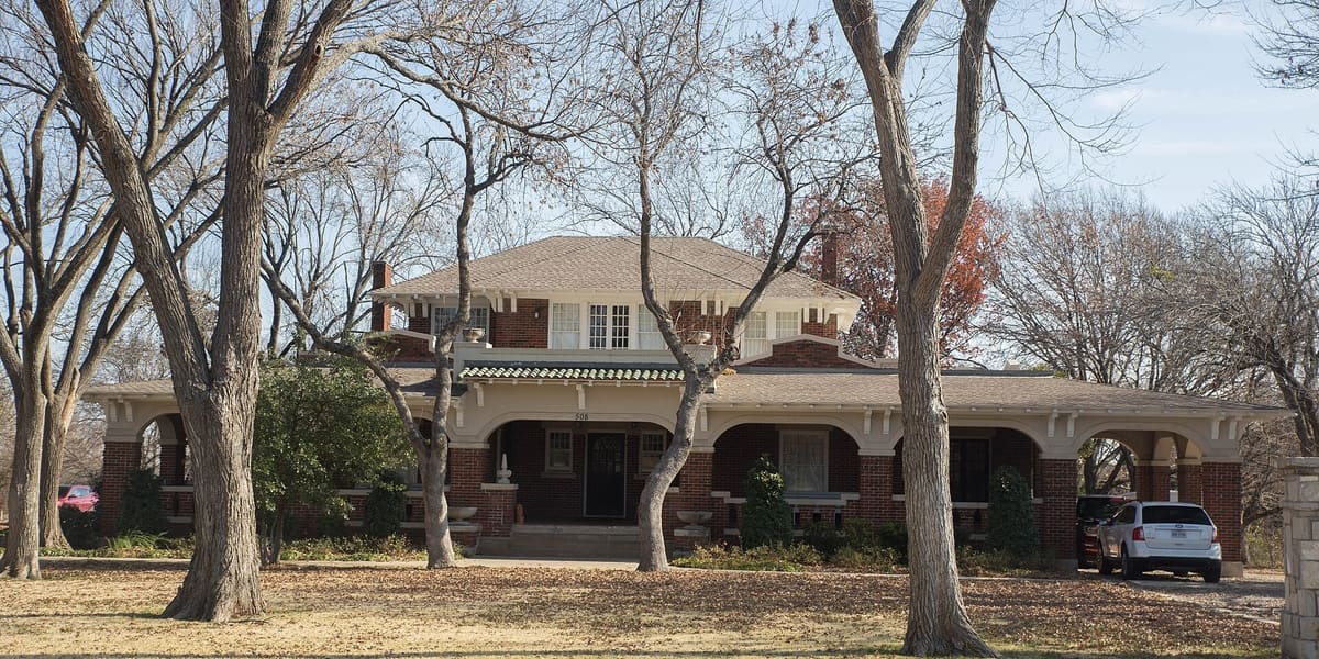 The red brick Trotter House in Midlothian with a wide arched front porch, a porte-cochere, and a hipped roof behind bare trees