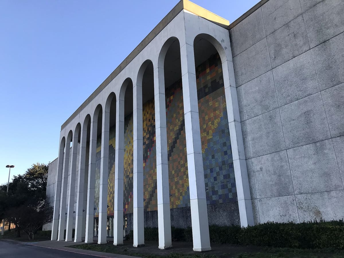 The arched concrete facade of the former Collin Creek Mall in Plano under a clear blue sky
