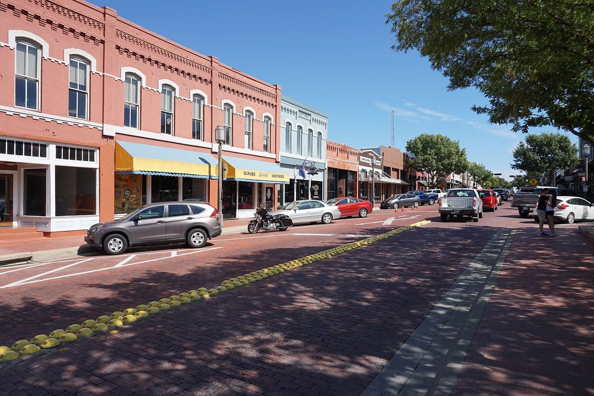 Two-story red brick storefronts with awnings along the brick-paved 15th Street in Downtown Plano