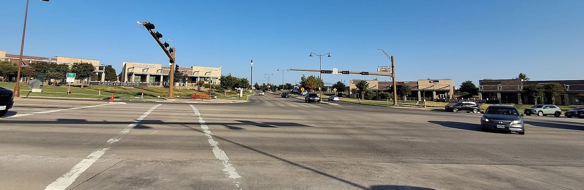 Gates of Prosper monument signs on two corners of a Preston Road intersection with stone-clad restaurant buildings behind them