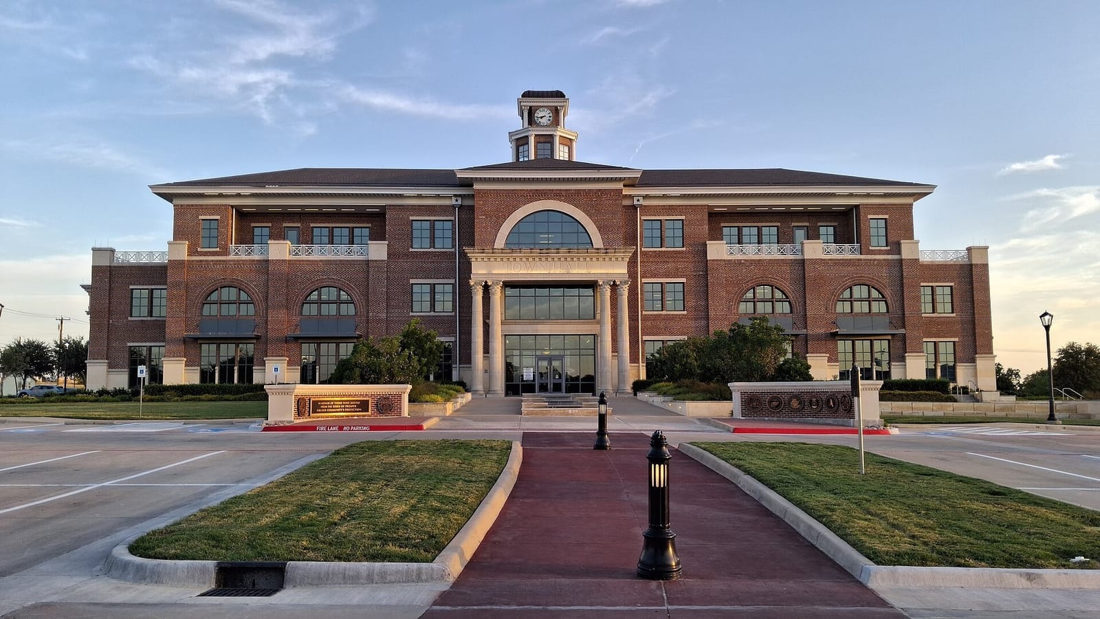 Prosper Town Hall, a three-story brick building with a clock cupola and a columned entrance, in evening light