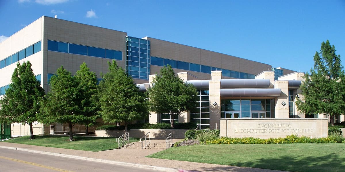 The Engineering and Computer Science Complex at The University of Texas at Dallas in Richardson, a long pale stone building with ribbon windows behind a row of young trees