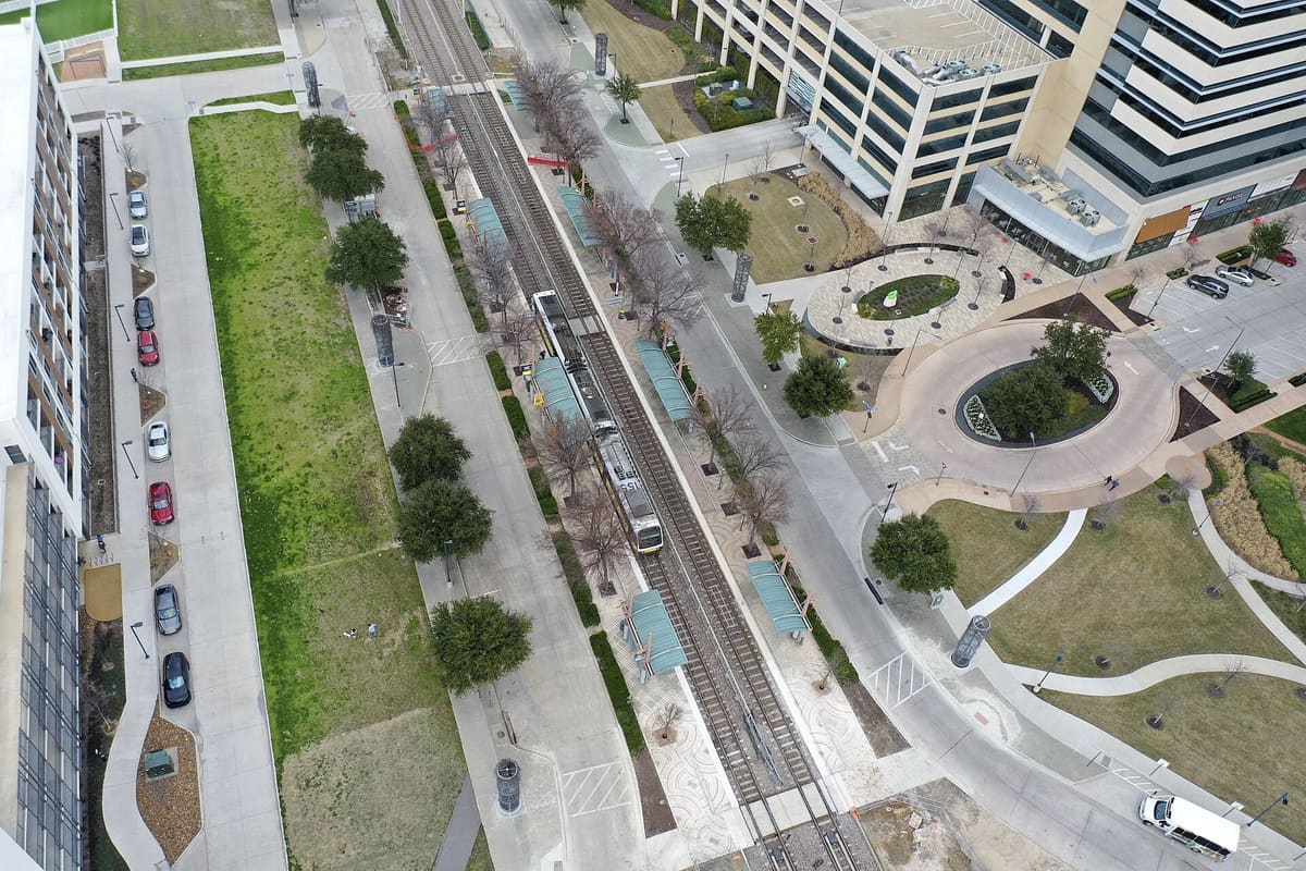 Aerial view of the CityLine/Bush DART station in Richardson, with a light rail train at the platform, office towers and ground-floor retail on the right, and an oval plaza and roundabout