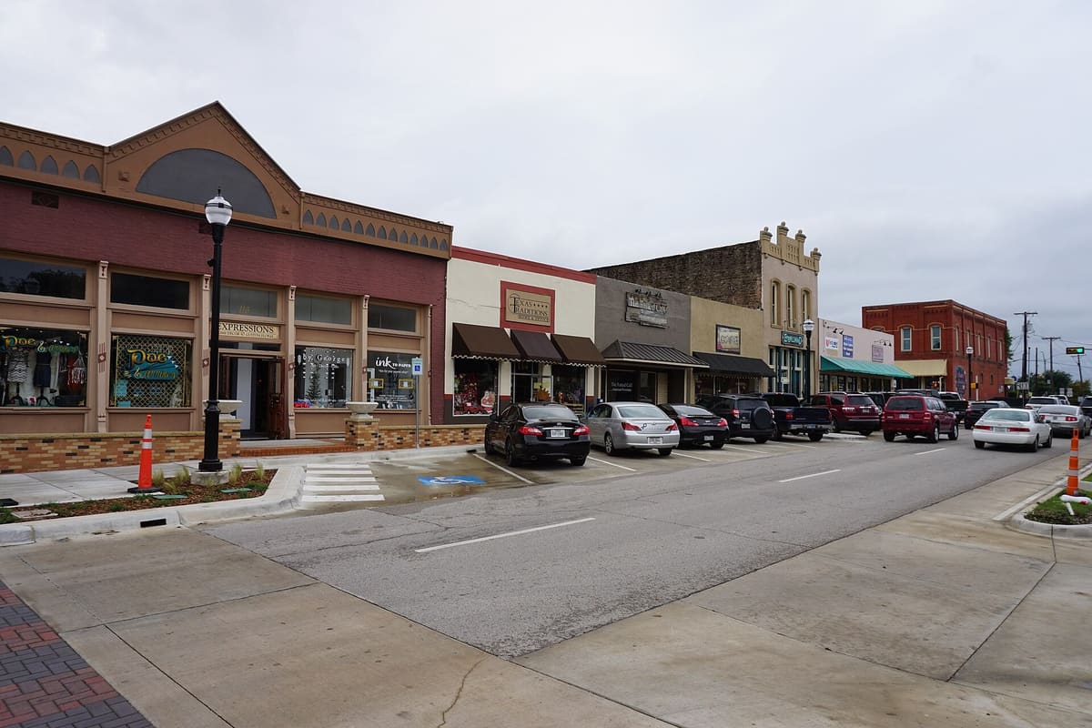 Brick and stucco storefronts with arched parapets, awnings, and angled parking on Rusk Street in downtown Rockwall, Texas