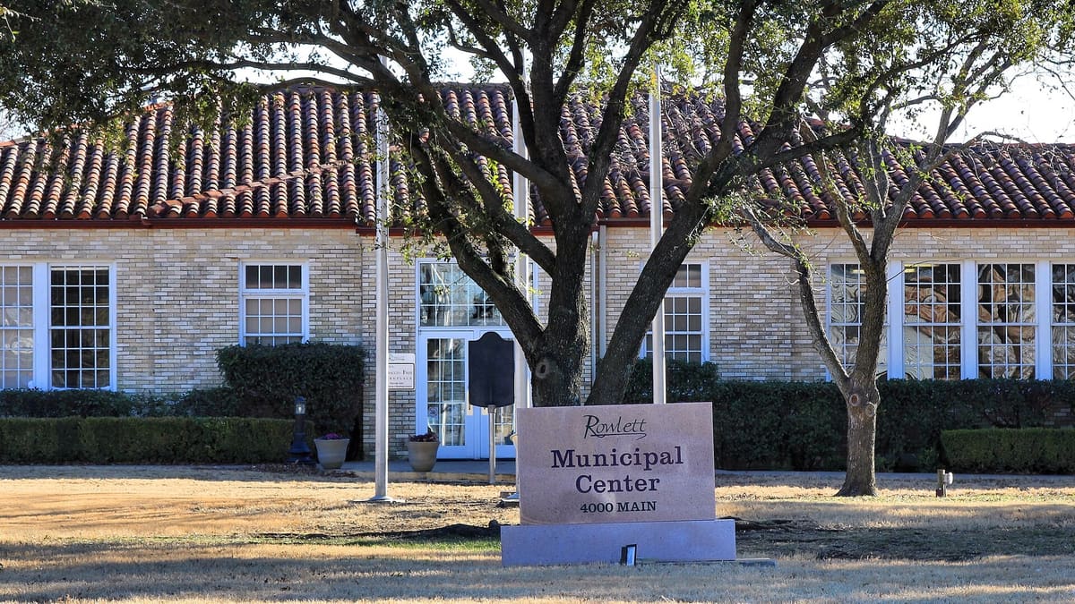 Rowlett Municipal Center at 4000 Main Street, a tan brick building with a red clay tile roof, white windows, oak trees, and a stone sign