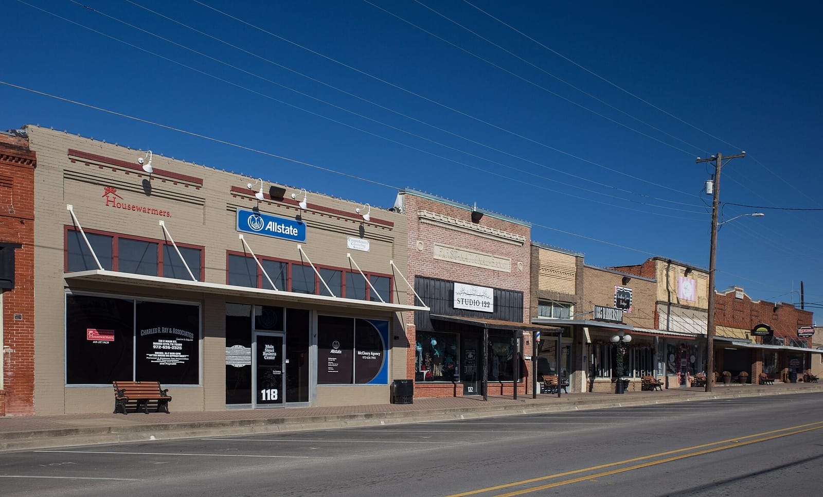 One-part brick commercial buildings on East Main Street in downtown Royse City, Texas, with metal canopies, a carved First National Bank panel, and a clear blue sky