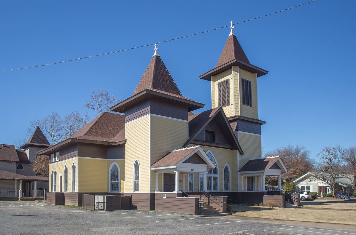The First United Methodist Church of Royse City in 2019, a yellow wood sanctuary with brown trim, two pointed towers of different heights, and arched stained glass windows