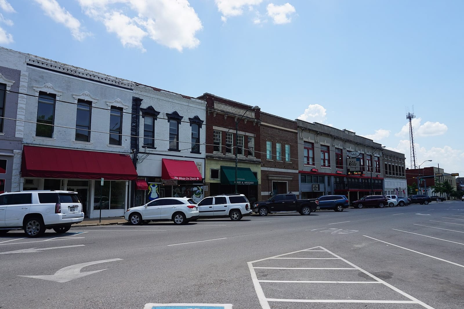 A row of two-story brick storefronts with red and green awnings on Travis Street in downtown Sherman, Texas, on a sunny day