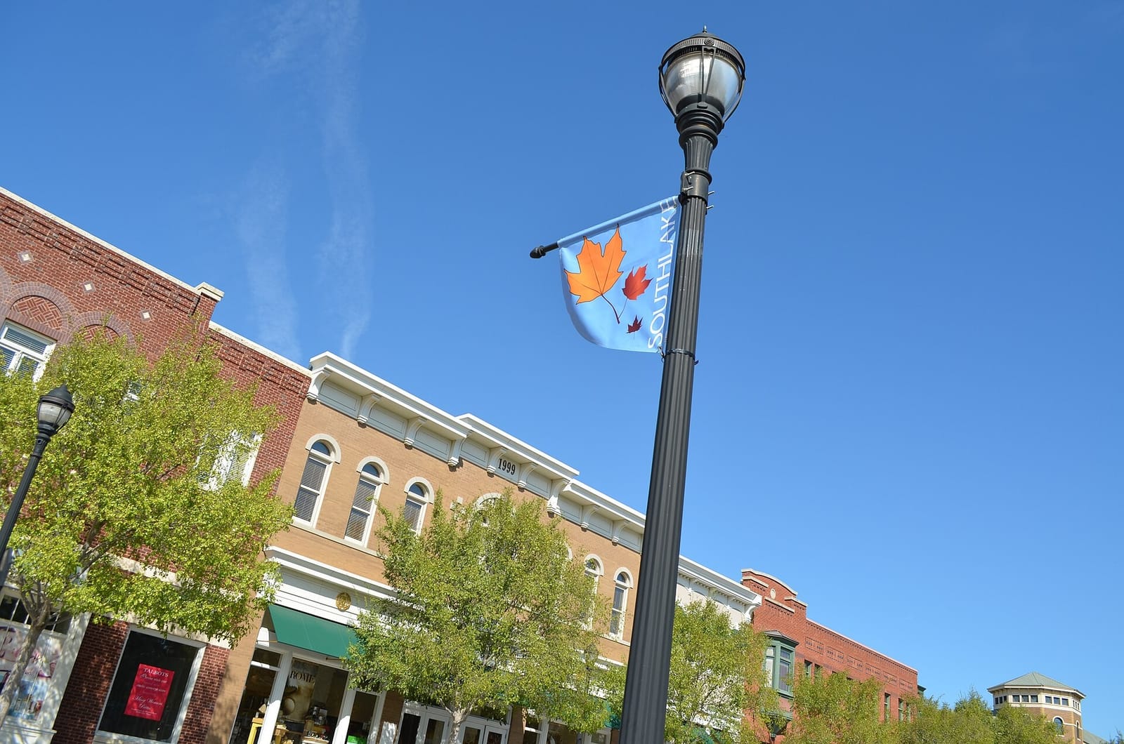 Two-story brick storefronts with arched windows and white cornices at Southlake Town Square in Southlake, Texas, behind a black lamp post flying a Southlake banner