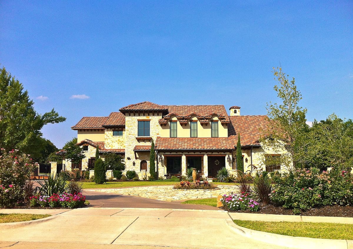 A two-story Mediterranean-style custom home in Southlake with cream stone and stucco walls, a terracotta tile roof, an arched wood door, and a circular stone motor court