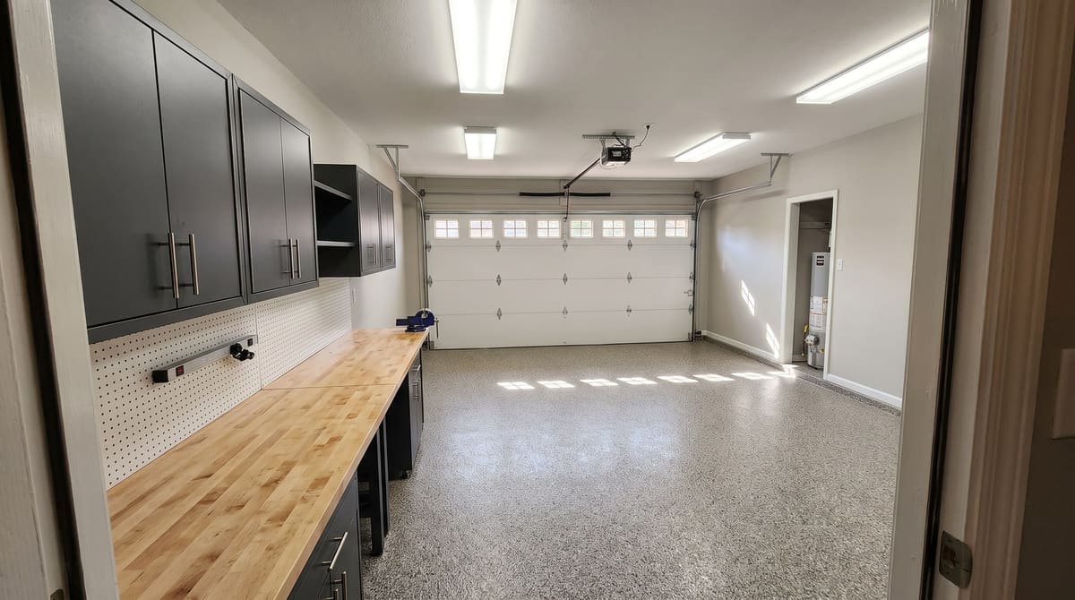 A two-car garage with a gray flake epoxy floor, charcoal wall cabinets, a butcher-block workbench, and LED shop lights