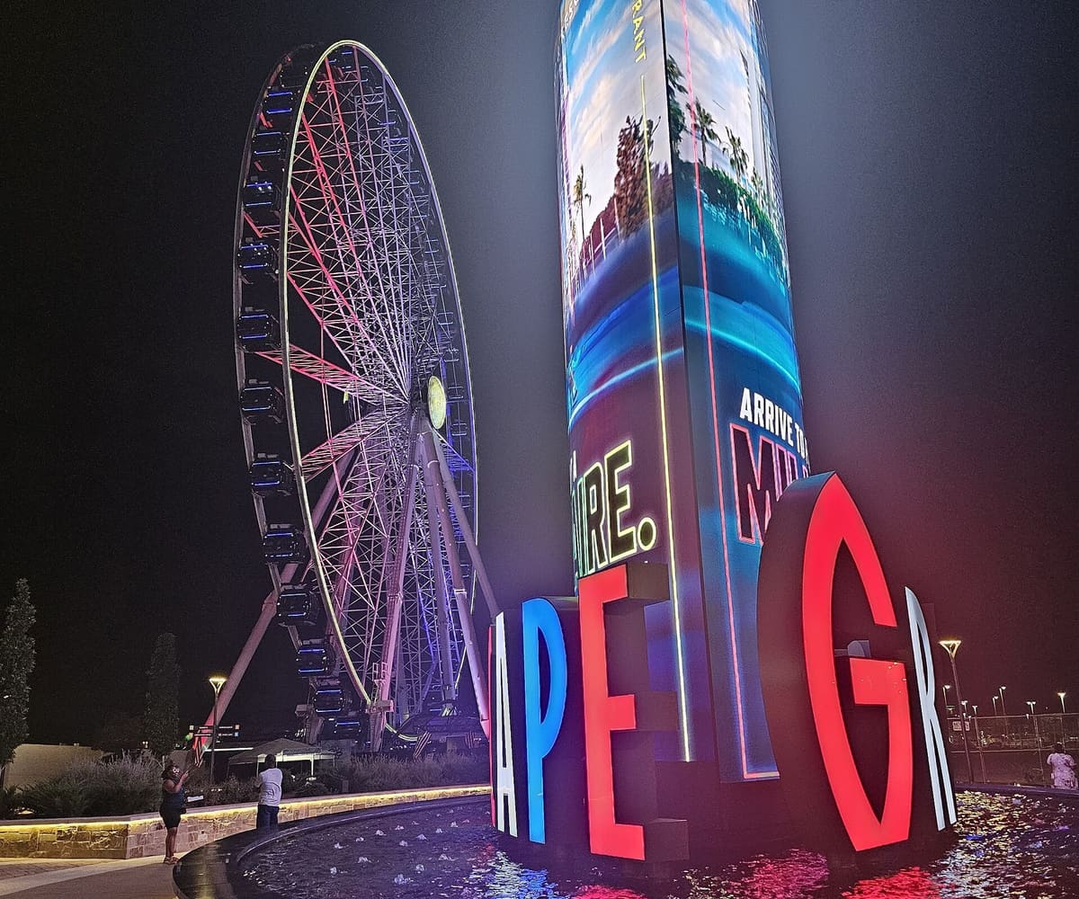 The lit Grandscape Ferris wheel at night beside the illuminated Grandscape letters and a fountain