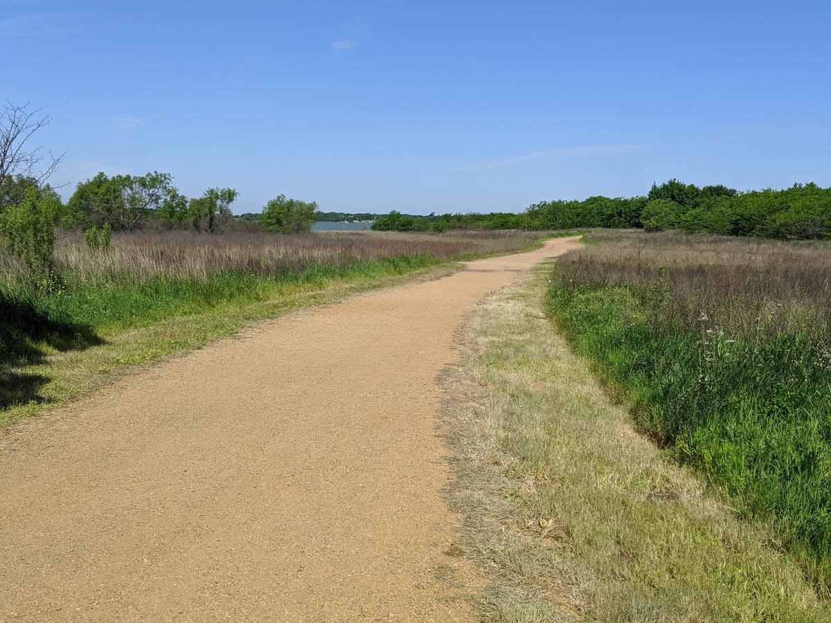A gravel trail through prairie grass and trees with Lewisville Lake visible ahead at Ridgepointe Park