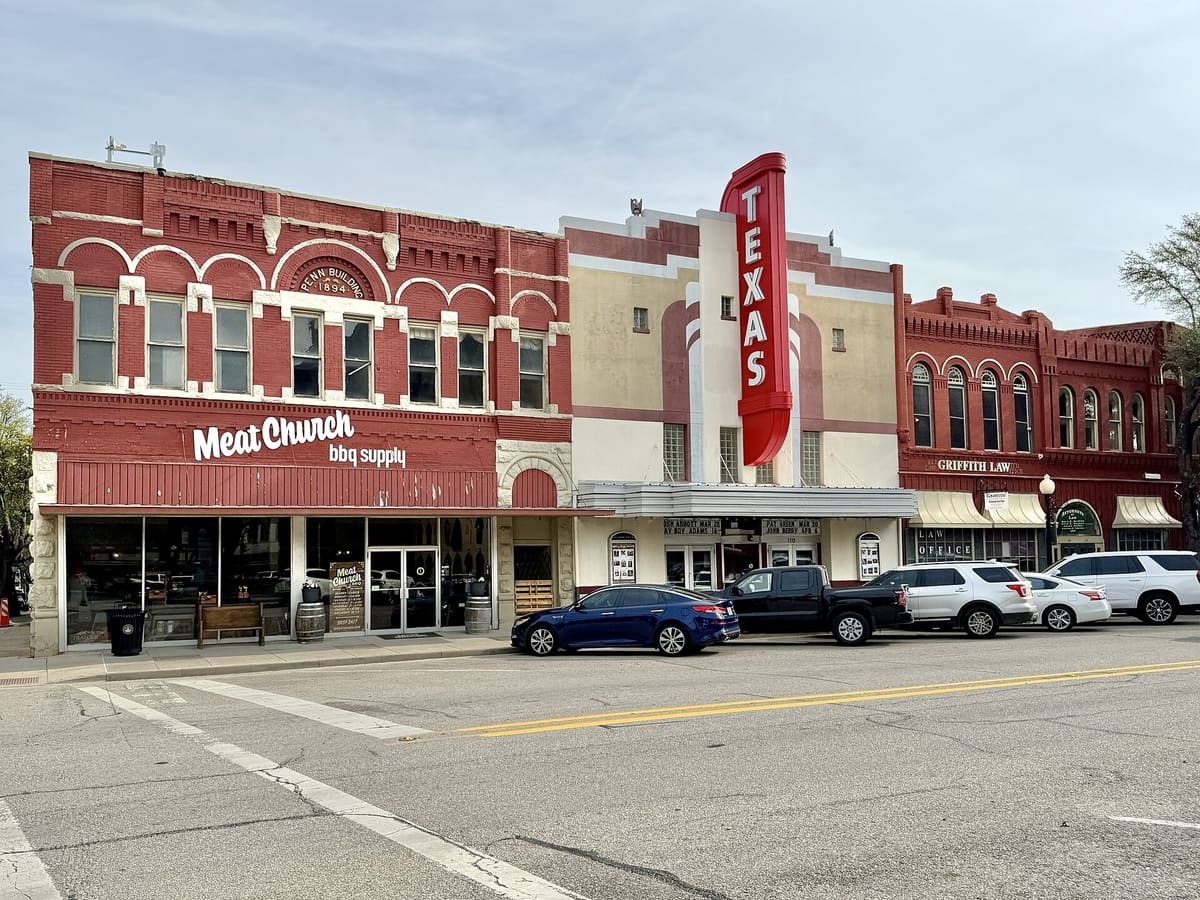 The 1894 Penn Building on the Waxahachie courthouse square, a red brick two-story block with white arched window hoods, beside the Texas Theatre and its tall red vertical sign
