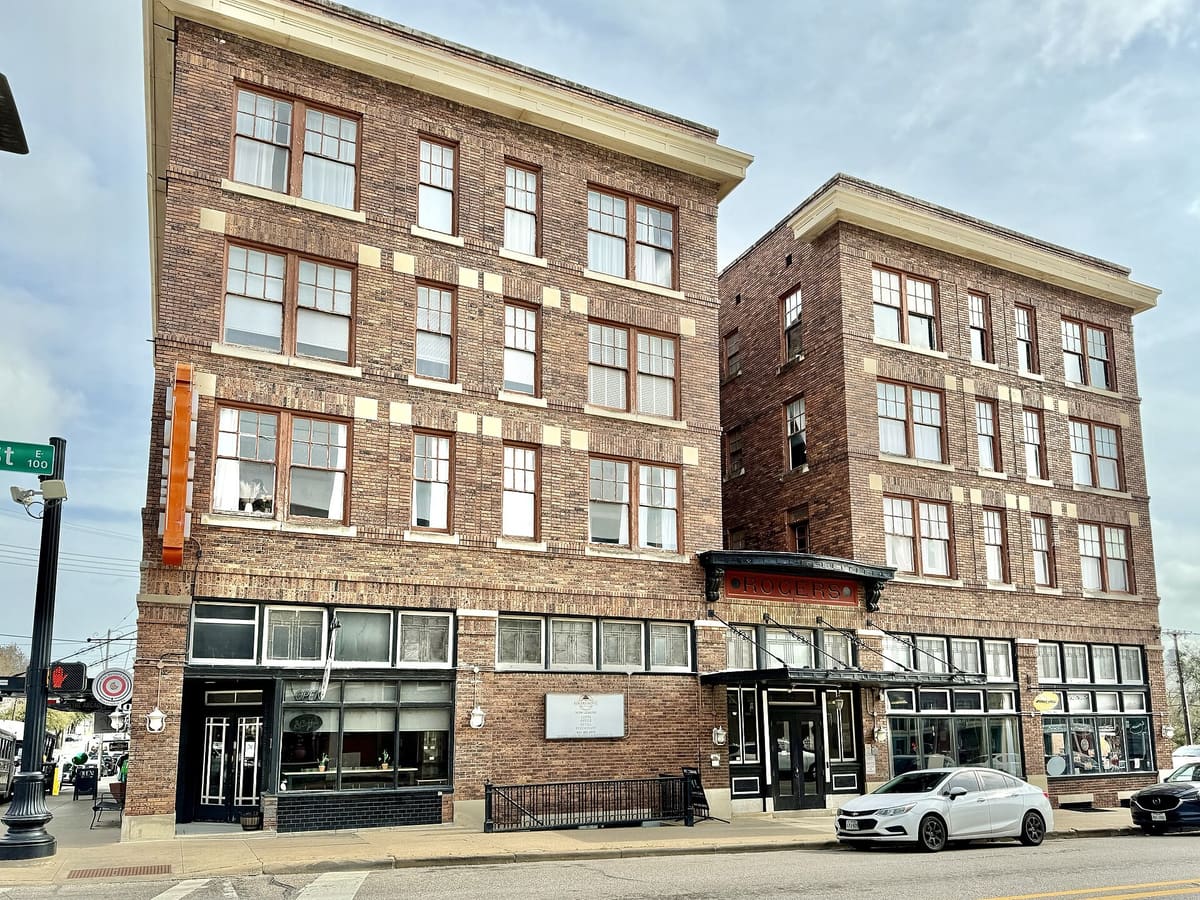 The Rogers Hotel in downtown Waxahachie, twin four-story dark brick towers with cream cornices, rows of wood windows, and ground-floor storefronts with a curved iron canopy